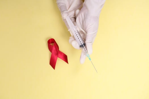red ribbon with medical gloves and syringe against HIV isolated on yellow background photo
