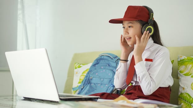 asian elementary school girl studying online listening from headphones at home photo