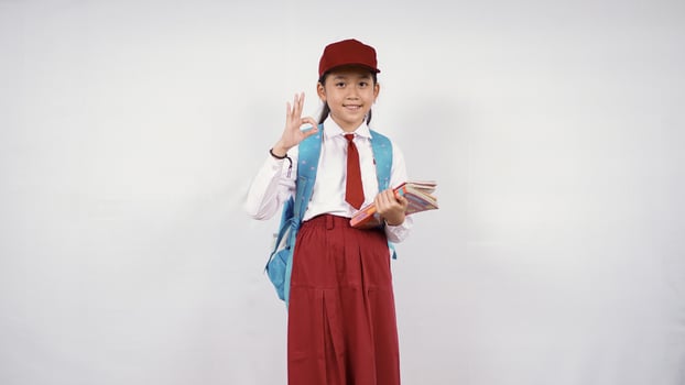 Asian elementary school girl going to leave with books and okay isolated on white background photo