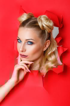 beautiful girl in Peeps out of the hole in red paper, beautiful bright make-up, facial expressions of surprise and interest. photo