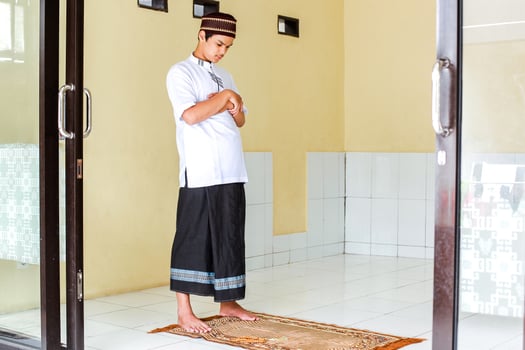 Portrait of young asian muslim man standing on the prayer mat with hand in chest are doing salat photo