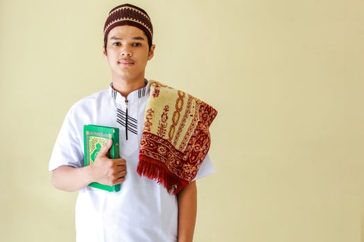 Portrait of young asian muslim holding the holy book Al-Quran and prayer mat on his shoulder get ready to pray photo