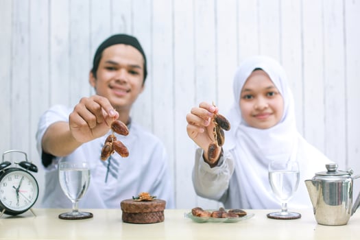 Blurry photo of muslim couple smiling and offering dates on hand into the camera selective focus on hands