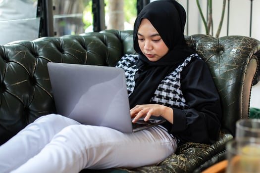 Asian Muslim woman relaxing on couch and working using laptop photo