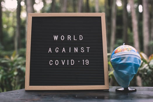 Quote on letter board says World Against Covid 19 and Earth globe in sterile medical mask with blurred nature background. photo