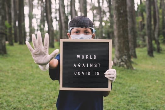 Asian boy wearing face masks and rubber hand glove standing with stop gesture in his hand while holding quote on letter board says World Against Covid 19 photo