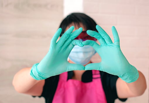 woman in glasses, apron, rubber gloves and mask showing sign love by her fingers. Health, healthcare, beauty industry, safety concept photo