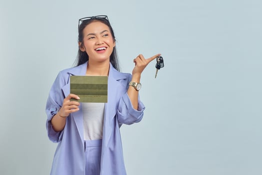 Portrait of cheerful young Asian woman showing vehicle book and holding vehicle keys isolated on white background photo