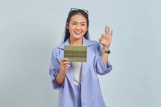 Portrait of smiling young Asian woman holding vehicle book and showing thumbs up gesture, Approving expression looking at camera showing success isolated on white background photo