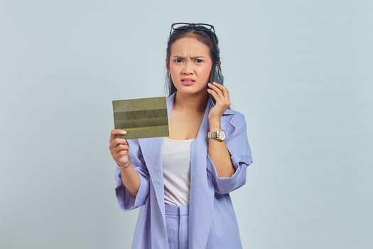 Portrait of pensive young Asian woman talking on mobile and showing vehicle book isolated on white background photo