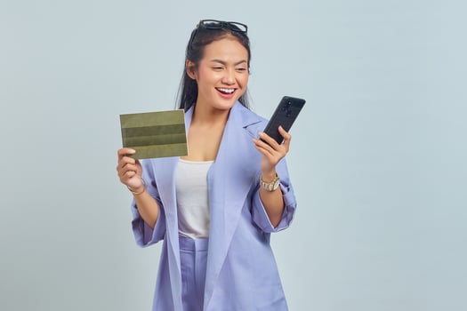 Portrait of cheerful young Asian woman showing vehicle book and using mobile phone isolated on white background photo