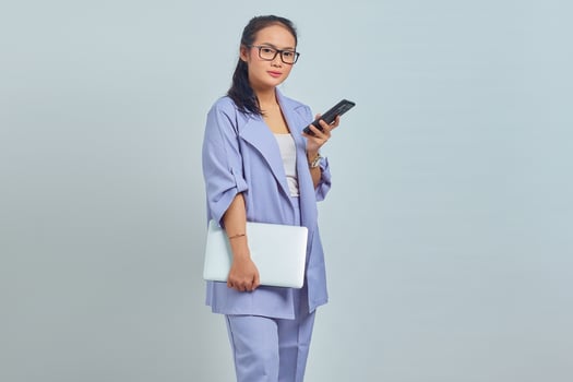 Portrait of pensive young Asian woman holding laptop and using mobile phone isolated on white background photo