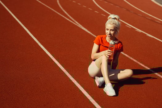 young beautiful blonde sits on a jogging track with a bottle of water in her hands photo