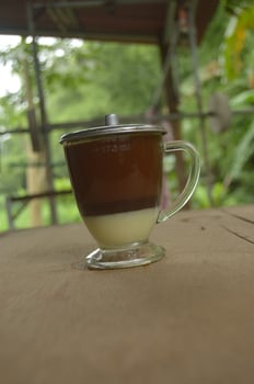 serving coffee with a clear glass and condensed milk underneath.  outdoor wooden background. photo