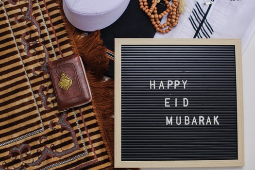 Top view of Muslim dress and praying beads with Holy Book of Al Quran and letter board says Happy Eid Mubarak. There is Arabic letter which means the holy book photo