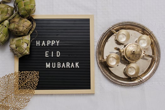 Top view of letter board says Happy Eid Mubarak and traditional food during lebaran celebration called ketupat with set golden teapot and cups photo
