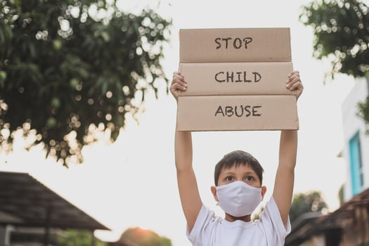 Asian boy in medical mask raising letter board says Stop Child Abuse when campaign photo