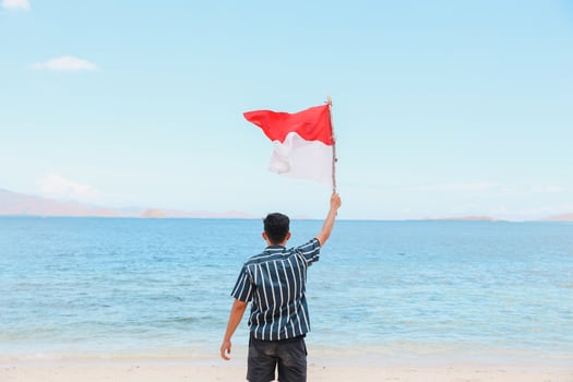 A man standing in the beach and waving Indonesian flag with seascape background photo