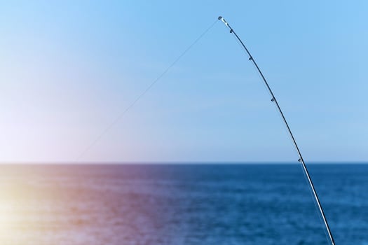 Fishing rod against blue ocean or sea background, copy space, Waiting for biggest haul, Meditative relax sport. photo