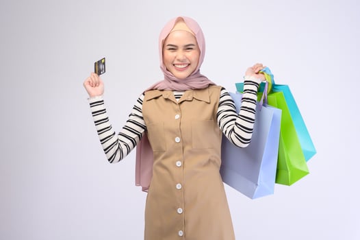 Young beautiful muslim woman in suit holding colorful shopping bags over white background studio photo
