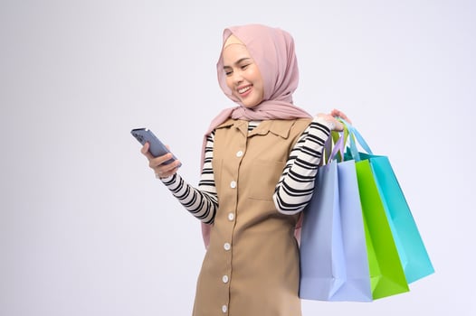 Young beautiful muslim woman in suit holding colorful shopping bags over white background studio photo