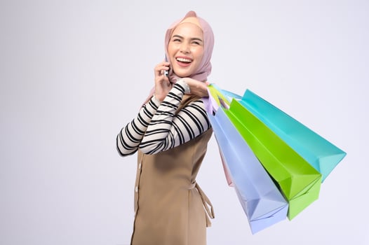 Young beautiful muslim woman in suit holding colorful shopping bags over white background studio photo