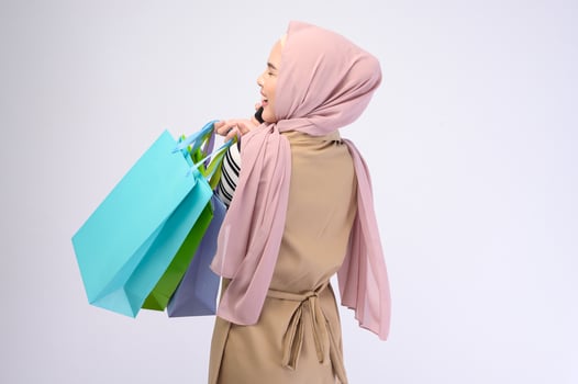 Young beautiful muslim woman in suit holding colorful shopping bags over white background studio photo