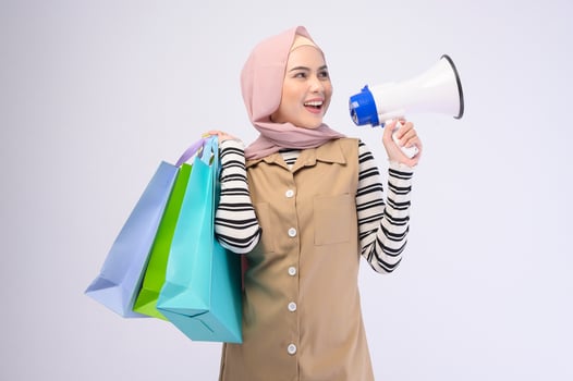 Young beautiful muslim woman in suit holding colorful shopping bags over white background studio photo