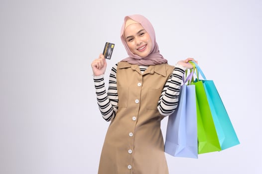 Young beautiful muslim woman in suit holding colorful shopping bags over white background studio photo