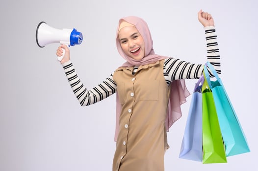 Young beautiful muslim woman in suit holding colorful shopping bags over white background studio photo