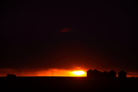Sun setting behind metal granaries in Saskatchewan photo