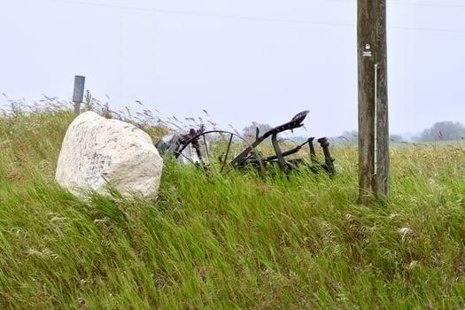 an old rusty plow sits in a weed filled field photo