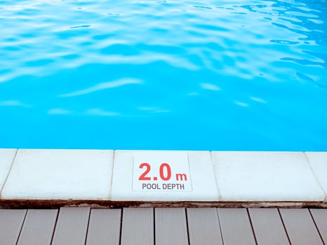The edge of the swimming pool with the table with information of the depth in English language. Sport, safety, recreation and relax concept. photo