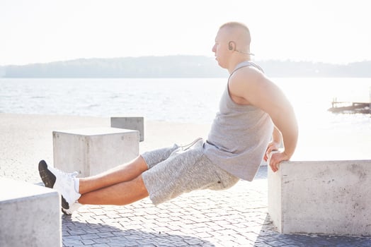 Profile view of a strong man exercising his arms and doing tricep dips outdoors in a park bench photo