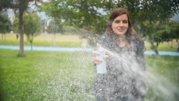 Hispanic woman shooting a stream of white foam from a spray can in the middle of a park photo
