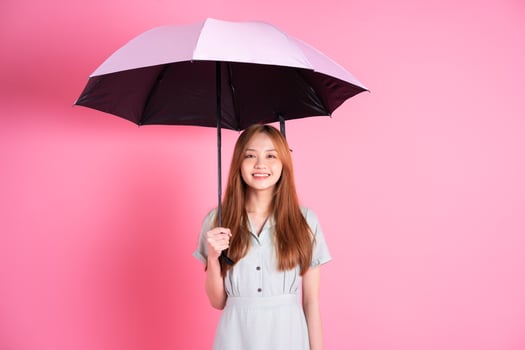 Young Asian woman holding umbrella on pink background photo