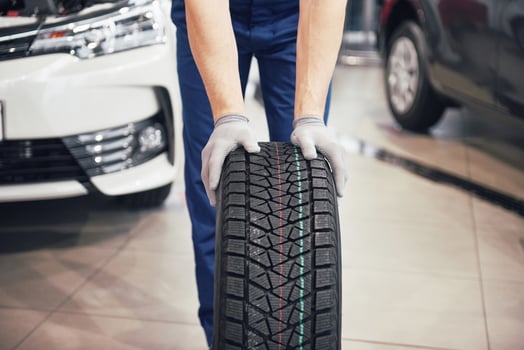 Closeup of mechanic hands pushing a black tire in the workshop photo