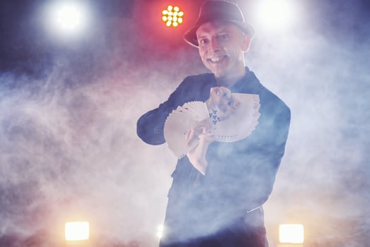 Magician showing trick with playing cards. Magic or dexterity, circus, gambling. Prestidigitator in dark room with fog photo