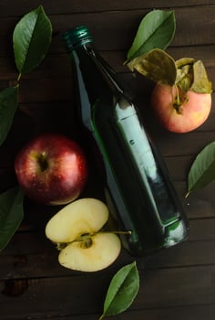 A bottle of a apple cider vinegar with fresh apples and green leaves. photo
