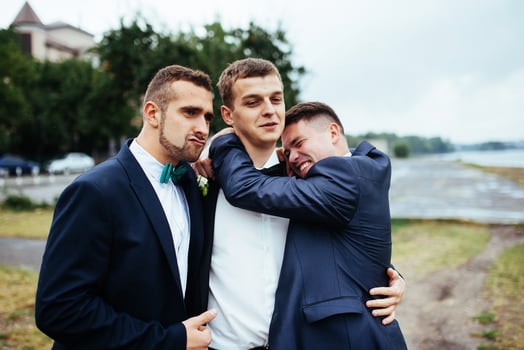 Confident smiling handsome groom in black suit with two groomsma photo