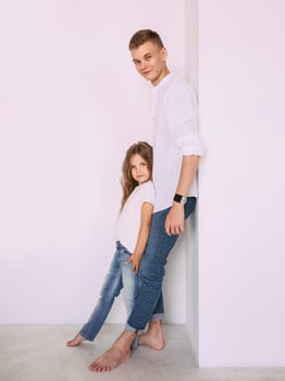 caucasian happy adorable siblings - teenager boy brother and little girl sister cuddling on white background indoor. Family, relationships, relatives, love, support concept photo