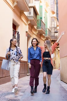 Satisfied young diverse women walking in old city district and laughing photo