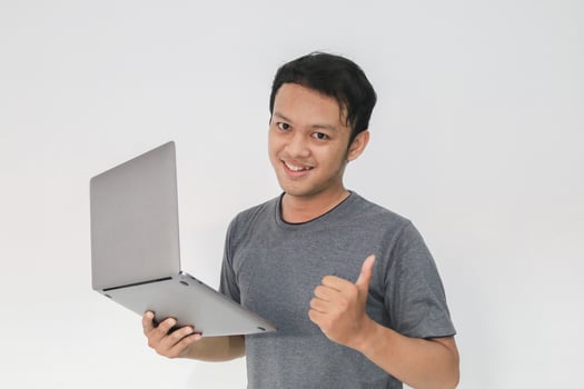 Young Asian man in grey t-shirt Feeling happy and smile with holding laptop in hand. photo