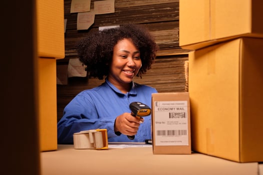 African American female worker in safety uniform using bar code scanner to check shipment orders at parcels warehouse, paper manufacture factory for the packing industry, logistic transport service. photo