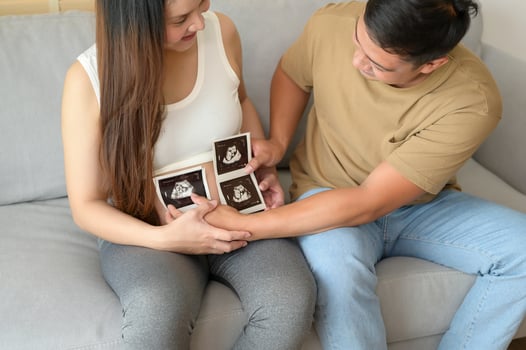 Young pregnant woman with husband holding ultrasound photo of newborn baby, maternity and family concept