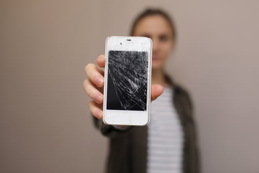 Frustrated young woman holding cellphone with broken screen glass. Phone display needs to repair. Isolated on gray background. selective focus on smartphone photo