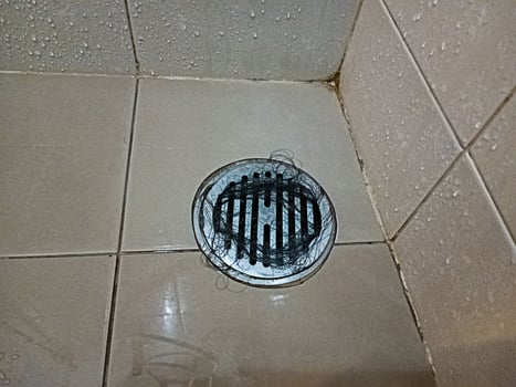 The bathroom tile floor has clogged hair that deposits the pipe. photo