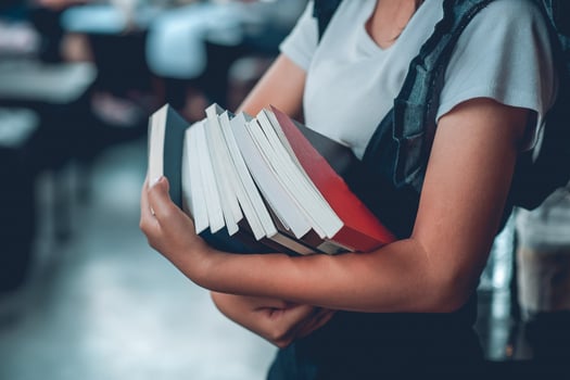 The girl holds many books and in the library. photo