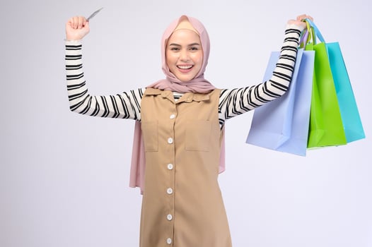 Young beautiful muslim woman in suit holding colorful shopping bags over white background studio photo