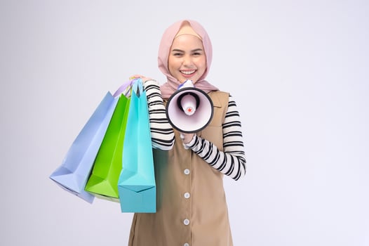 Young beautiful muslim woman in suit holding colorful shopping bags over white background studio photo
